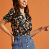 Woman wearing a vintage inspired colorful patterned top and blue jean skirt against an orange background