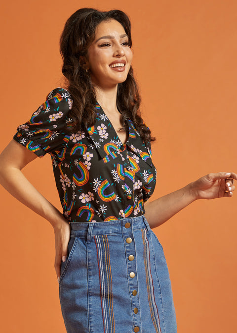 Woman wearing a vintage inspired colorful patterned top and blue jean skirt against an orange background