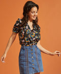 Woman wearing a rainbows and flower patterned top and denim skirt against an orange background