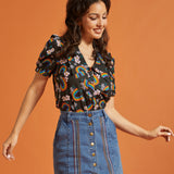 Woman wearing a rainbows and flower patterned top and denim skirt against an orange background