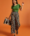 Woman holding a boombox while wearing a retro green tee and rainbow print pants
