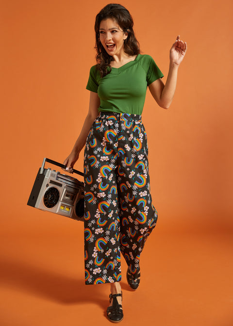 Woman holding a boombox while wearing a retro green tee and rainbow print pants