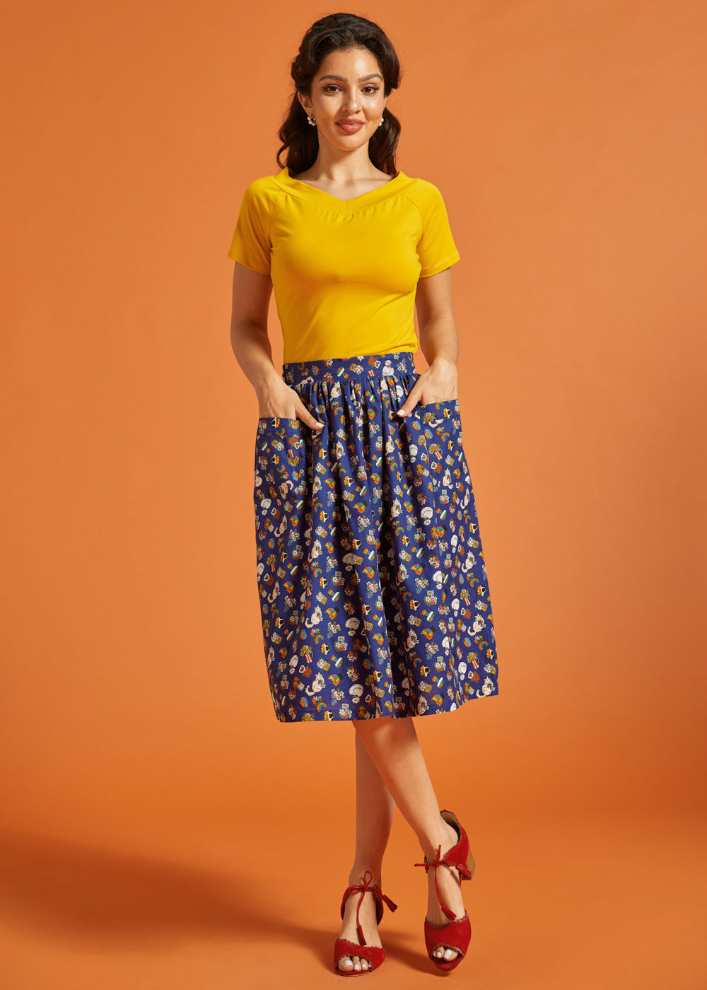 Woman wearing a yellow top and blue printed skirt on an orange background