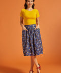 Woman wearing a yellow top and blue printed skirt on an orange background