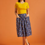 Woman wearing a yellow top and blue printed skirt on an orange background