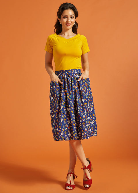 Woman wearing a yellow top and blue printed skirt on an orange background