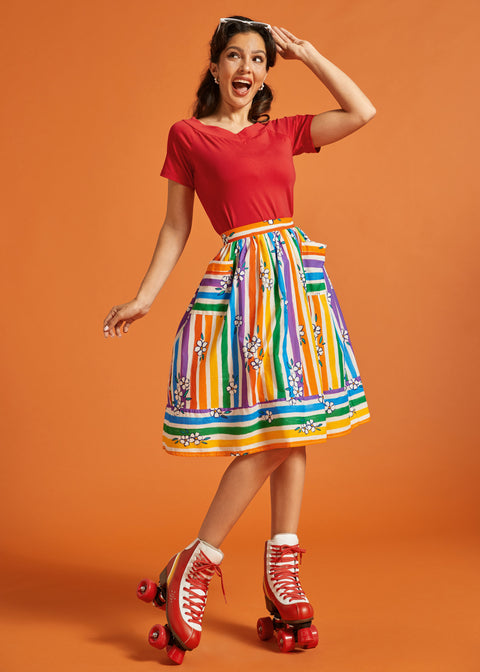 Woman wearing a red top and colorful striped skirt with roller skates on an orange background