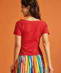 Back view of a woman wearing a red top and colorful striped skirt against an orange background