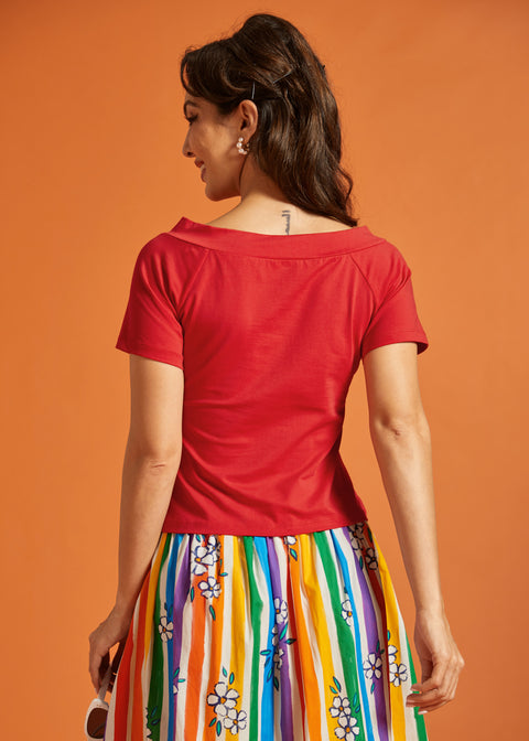 Back view of a woman wearing a red top and colorful striped skirt against an orange background