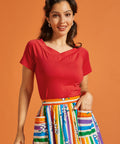 Woman wearing a red top and colorful striped skirt against an orange background