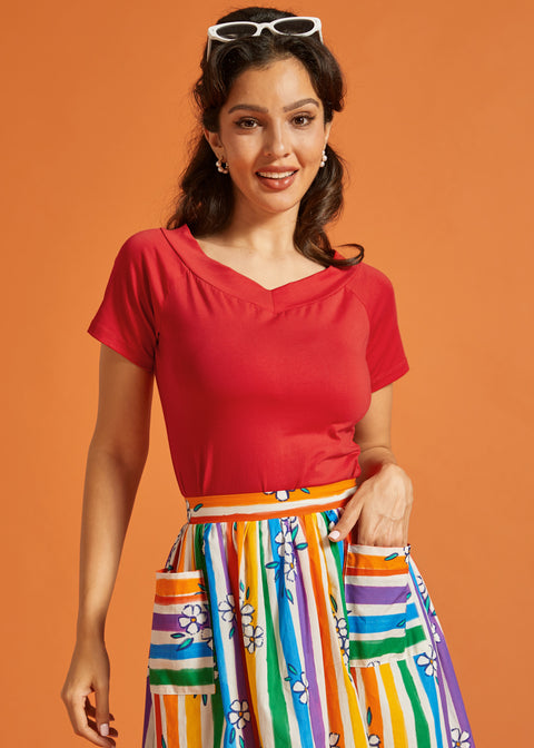 Woman wearing a red top and colorful striped skirt against an orange background