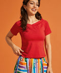 Woman wearing a red top and colorful striped skirt against an orange background