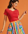 Woman wearing a red top and colorful striped skirt against an orange background