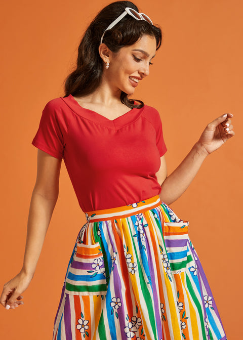 Woman wearing a red top and colorful striped skirt against an orange background