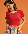 Woman wearing a red v-neck top and colorful skirt against an orange background
