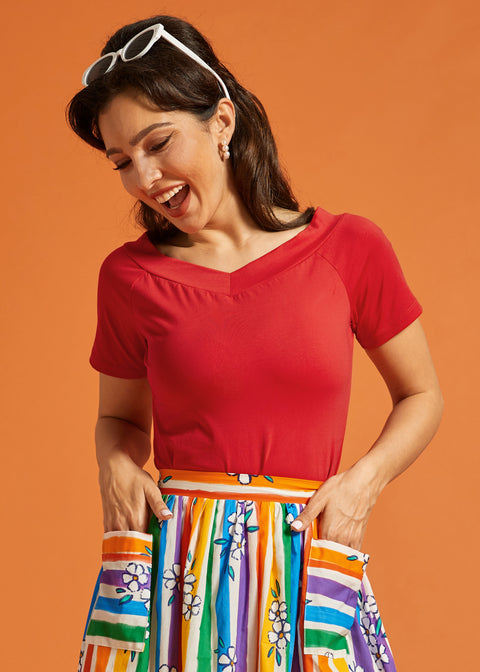 Woman wearing a red v-neck top and colorful skirt against an orange background