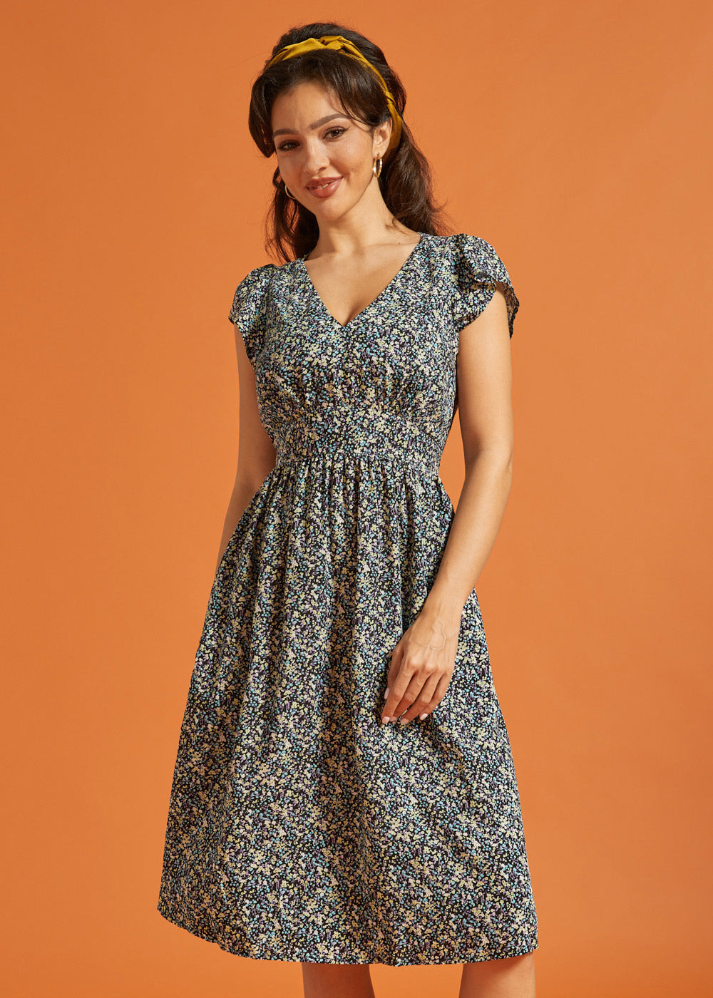 Woman wearing a black floral fit-and-flare dress with flutter sleeves and pockets