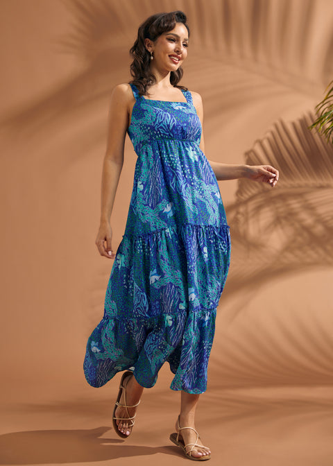 Woman wearing a blue tropical print tiered maxi dress with square neckline and open-back bow