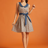 Woman wearing a vintage-inspired sleeveless fit-and-flare dress with a colorful horseshoe print, oversized blue Peter Pan collar, and matching tie belt.