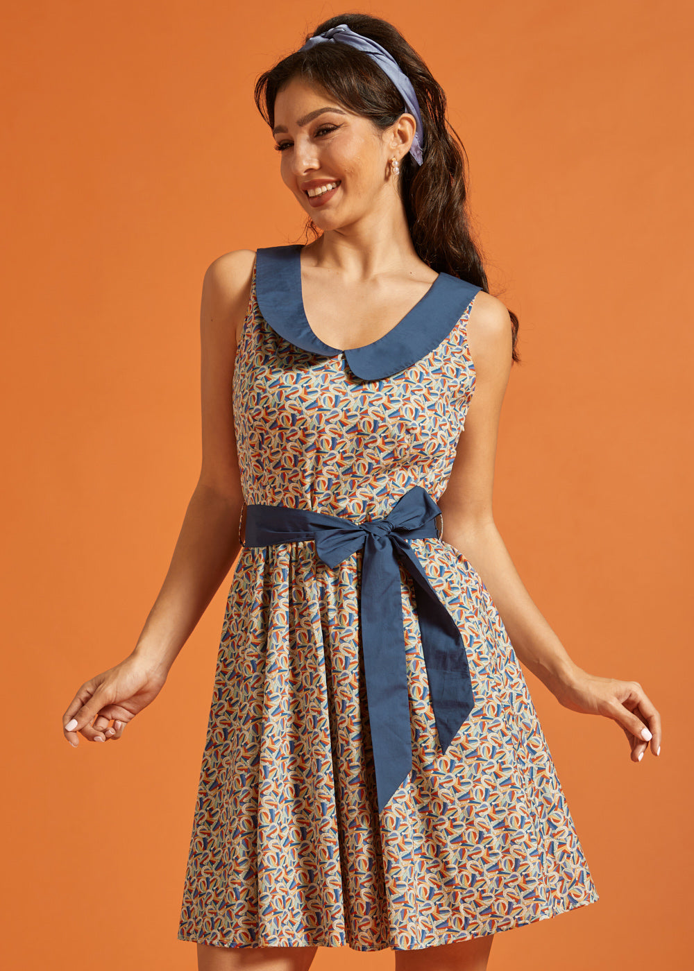 Front view of a cotton fit-and-flare dress featuring a novelty horseshoe print, contrast Peter Pan collar, and removable blue waist sash.