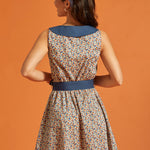 Back view of a retro-inspired sleeveless horseshoe print dress with a statement blue collar and coordinating tie belt.