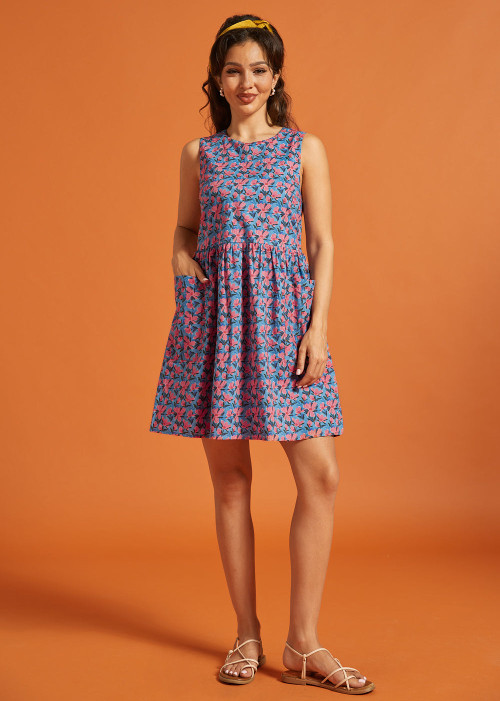 Woman modeling a sleeveless cotton shift dress with pink floral print and patch pockets.