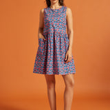 Woman modeling a sleeveless cotton shift dress with pink floral print and patch pockets.