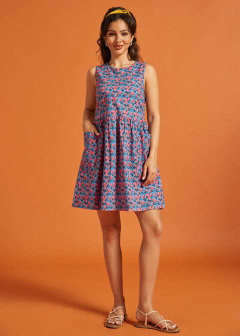 Woman modeling a sleeveless cotton shift dress with pink floral print and patch pockets.