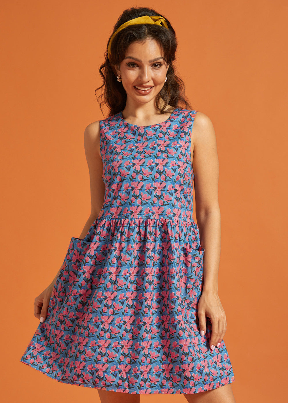 Woman wearing a sleeveless blue and pink floral A-line dress with oversized patch pockets.