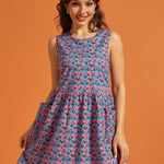 Woman wearing a sleeveless blue and pink floral A-line dress with oversized patch pockets.