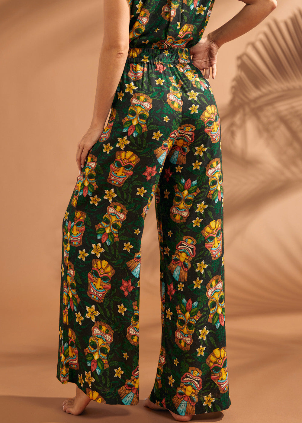 Woman wearing tiki print wide leg pants showing comfortable elastic back waistband.