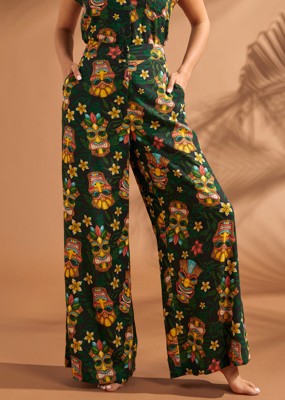 Woman wearing black tropical tiki print wide leg pants with side pockets.