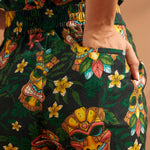 Close-up of colorful tiki mask and floral novelty print on black linen blend trousers.