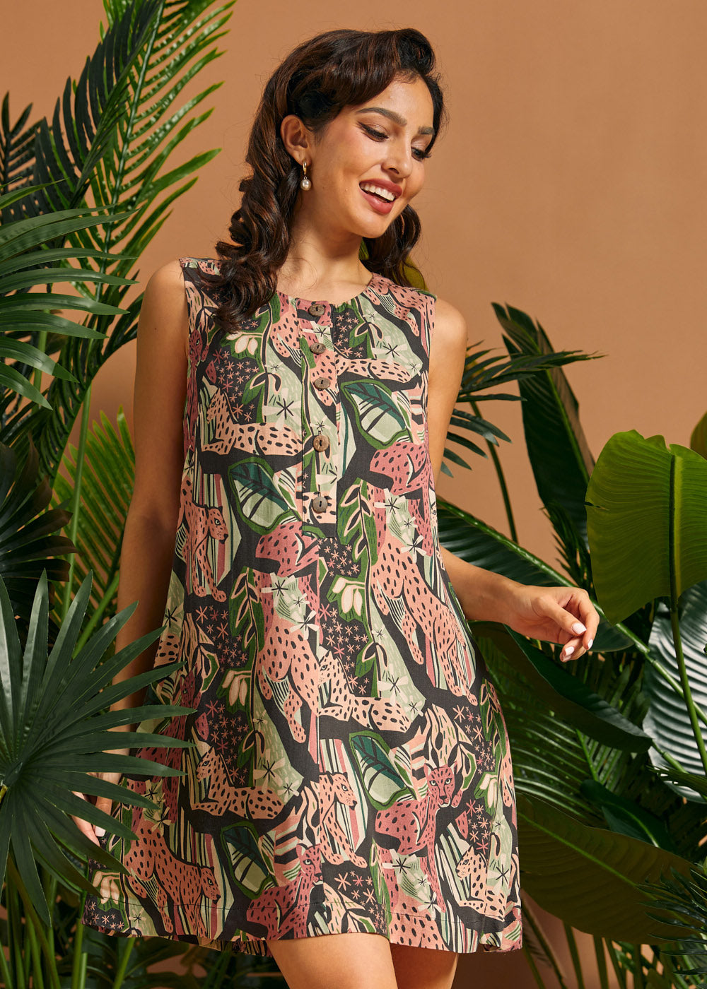 Woman wearing a sleeveless A-line mini dress with retro jungle print and decorative front buttons.