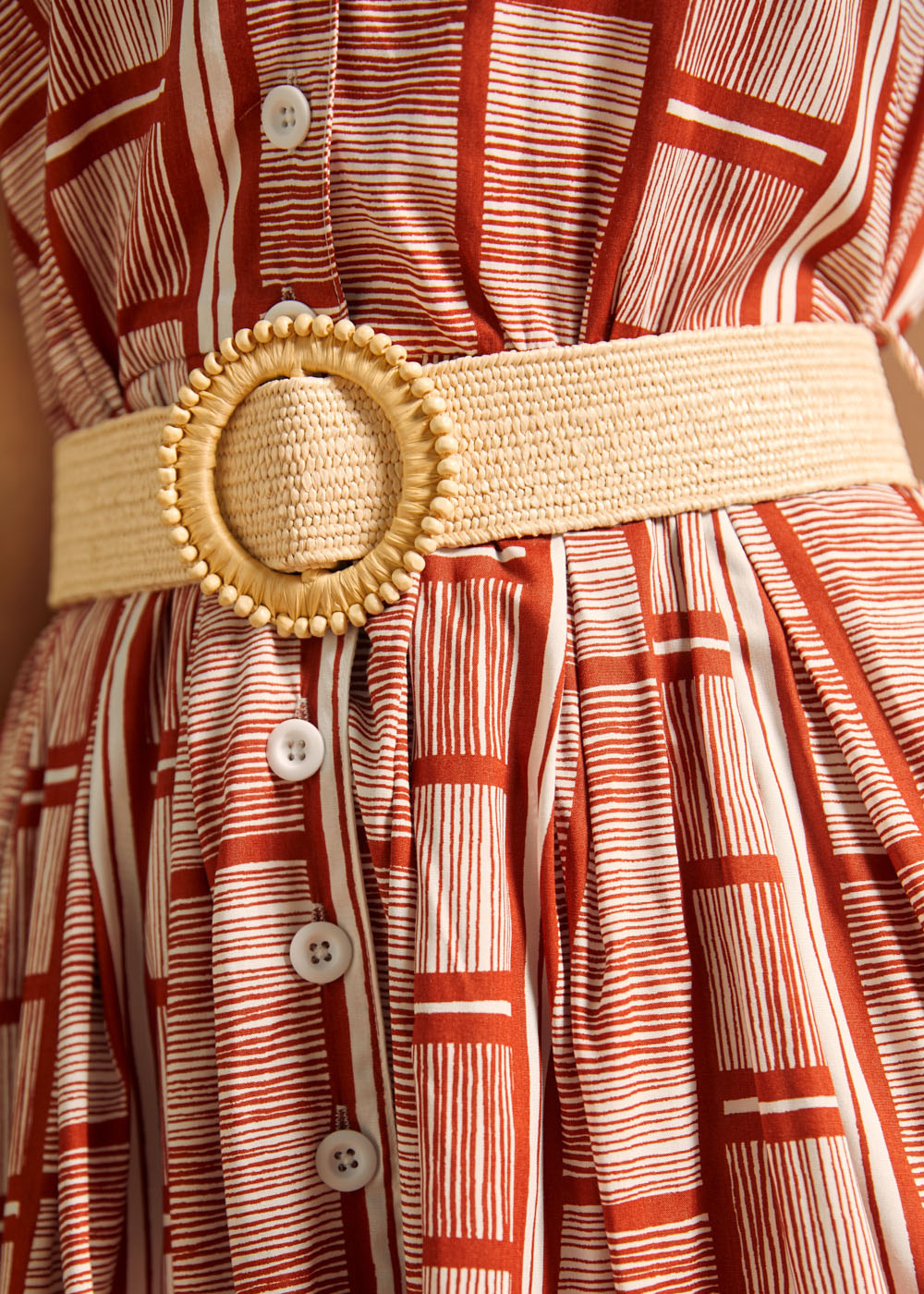 Detail of woven belt and button placket on terracotta print dress.