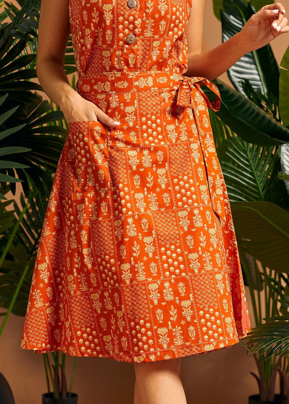 Woman wearing an orange cotton wrap skirt with adjustable tie waist and patch pocket.