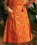 Woman wearing an orange cotton wrap skirt with adjustable tie waist and patch pocket.