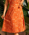 Woman wearing an orange patterned dress with plants in the background