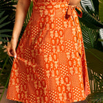 Woman wearing an orange patterned dress with plants in the background