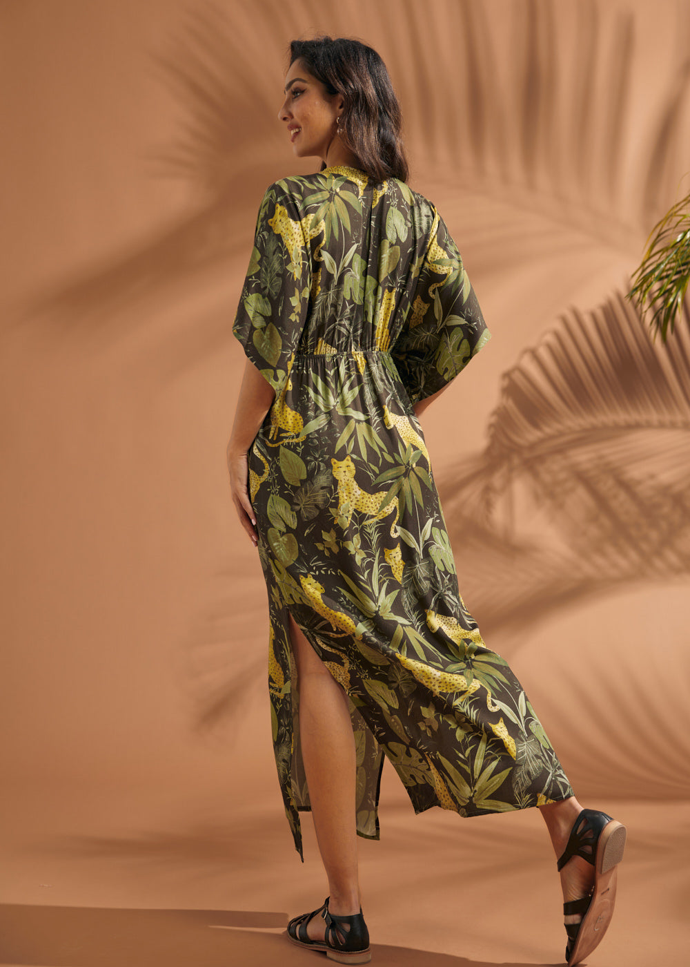 Back view of a woman wearing a tropical print maxi dress with elasticized waist and side slit.