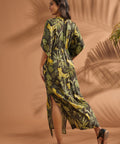 Back view of a woman wearing a tropical print maxi dress with elasticized waist and side slit.