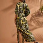 Back view of a woman wearing a tropical print maxi dress with elasticized waist and side slit.