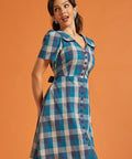 Woman wearing a retro blue checkered cotton dress with short puff sleeves and removable sash belt