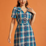 Front view of blue plaid fit-and-flare shirt dress featuring fabric-covered buttons and tie waist