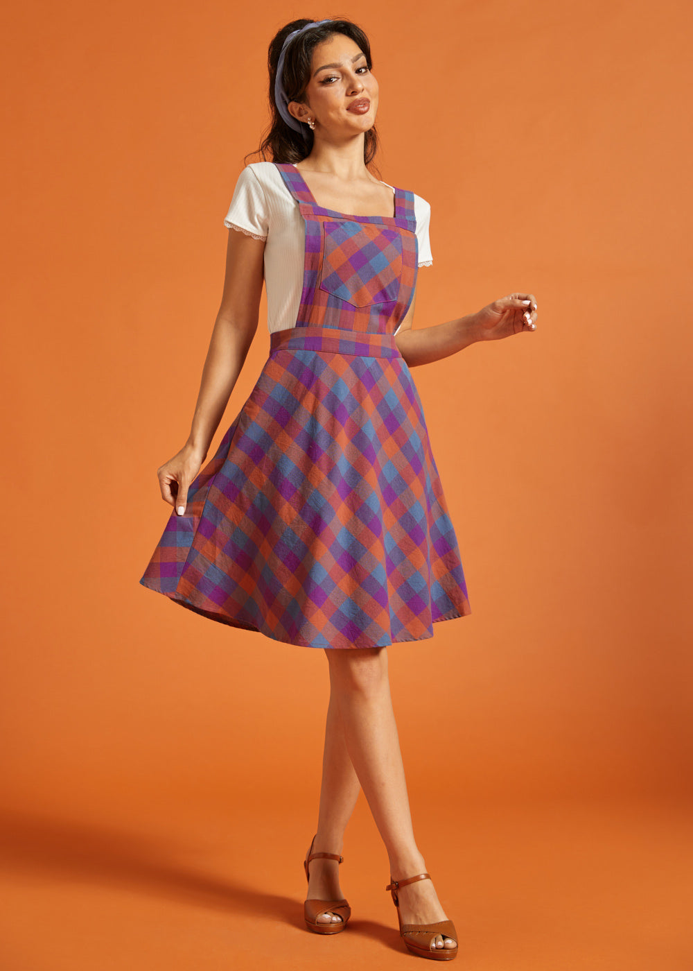 Woman wearing retro-inspired plaid pinafore dress with front bib pocket