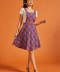 Woman wearing retro-inspired plaid pinafore dress with front bib pocket