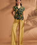 Woman wearing black novelty tiki print blouse paired with mustard wide leg pants.