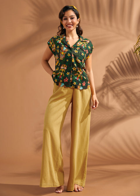 Woman wearing black novelty tiki print blouse paired with mustard wide leg pants.