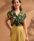 Woman wearing tropical tiki print button front blouse with cap sleeves and camp collar.