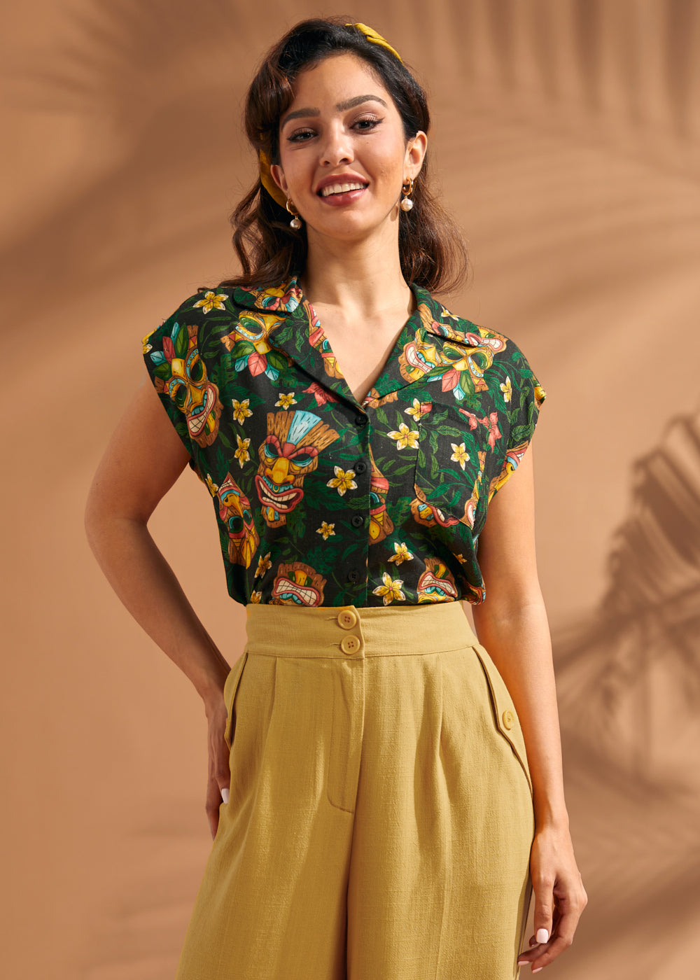 Woman wearing tropical tiki print button front blouse with cap sleeves and camp collar.